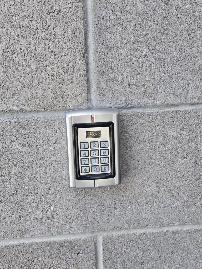 A metallic keypad access control panel by Resolute Technology LLC is mounted on a gray concrete wall, featuring numbers 0-9, function keys, and neatly organized cabling and wire connections.