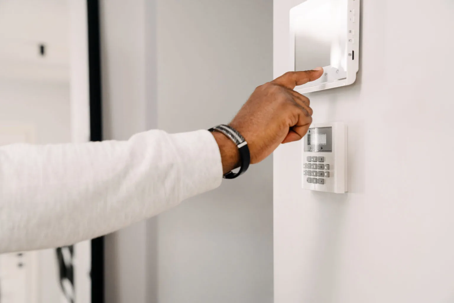 A person’s hand is pressing a button on a wall-mounted commercial security system keypad and touchscreen panel, possibly linked to CCTV cameras or controlled by a wire connection.