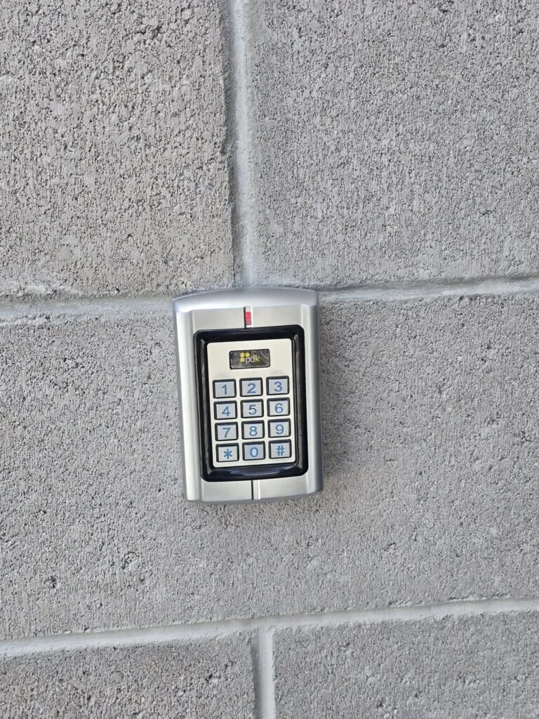 A metallic keypad access control panel by Resolute Technology LLC is mounted on a gray concrete wall, featuring numbers 0-9, function keys, and neatly organized cabling and wire connections.